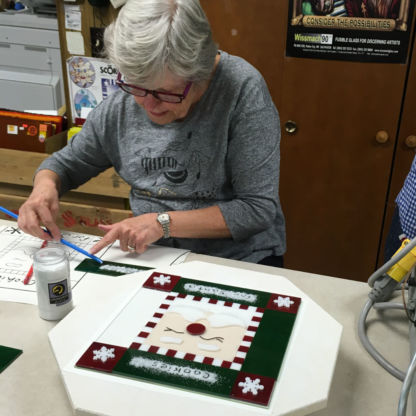 Fused christmas cookie tray class student placing glass frit on Santa project