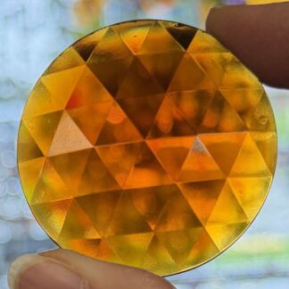 Round, faceted orange-yellow gemstone held between fingers, close-up view.