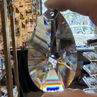 Close-up of a large, kaleidoscopic crystal prism being held by fingers in a shop, with vivid rainbow light refracted through its facets.