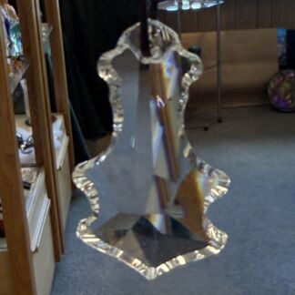 Crystal trophy with irregular, scalloped edges, hanging from a rod in a room; facets catch light and create rainbow reflections.
