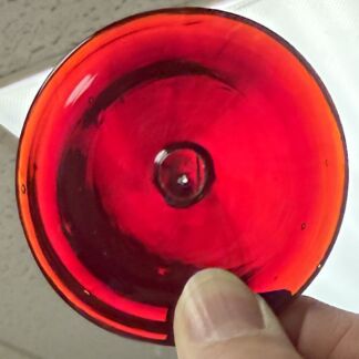 Close-up of a red circular glass lens/reflector being held by a finger
