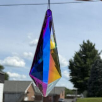 Colorful diamond-shaped crystal ornament hanging outdoors against a blue sky with houses in the background