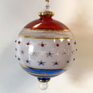 Hanging glass Christmas ornament with a red top, white middle with silver stars and gem accents, and a blue bottom.