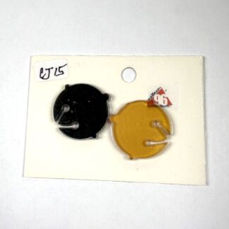 Two circular enamel pins, one black and one mustard yellow, mounted on a white display card.