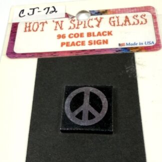 Label reads 'HOT N SPICY GLASS' with '96 COE BLACK PEACE SIGN' and 'Made in USA' on a colorful border; a peace-sign tile sits on a black surface below the tag.