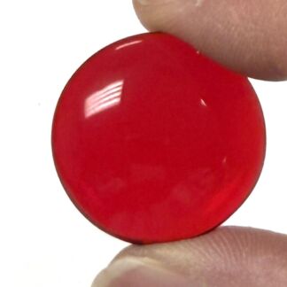 Glossy red circular disc held between a thumb and finger (close-up).