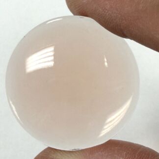 Close-up of a smooth, pale pink sphere being held between two fingers.