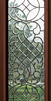 Tall vertical stained-glass window with intricate geometric and scroll motifs in a dark wood frame; garden with trees visible outside.