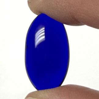 Blue oval glass gem being held between two fingertips.