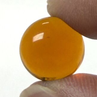 Close-up of a glossy orange-yellow round bead held between a thumb and finger.