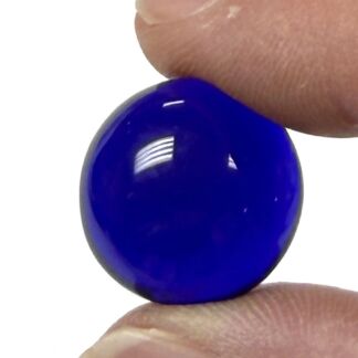 Small, round cobalt blue glass bead being pinched between fingertips, showing a glossy, reflective surface.