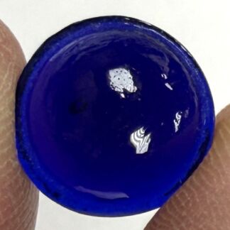 Blue cobalt bottle cap held between two fingers, close-up view with glossy surface reflecting light.