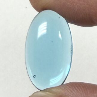 Light blue oval polished gemstone held between thumb and index finger.