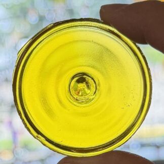 Close-up of a yellow glass bottle cap held between two fingers.